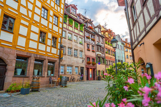 Vibrant afternoon street view of historic half-timbered medieval houses, a cobblestone alley, and blooming pink flowers in the old town of Nuremberg