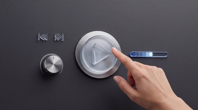 Close-up of a human hand pressing a transparent glass play button on a futuristic control panel with metal dials and digital status indicators for automation and multimedia control.