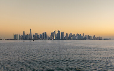 Panoramic view of Doha West Bay skyline reflecting golden sunrise light across calm bay waters in Qatar. © fornax