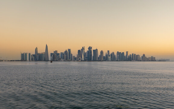 Panoramic view of Doha West Bay skyline reflecting golden sunrise light across calm bay waters in Qatar.