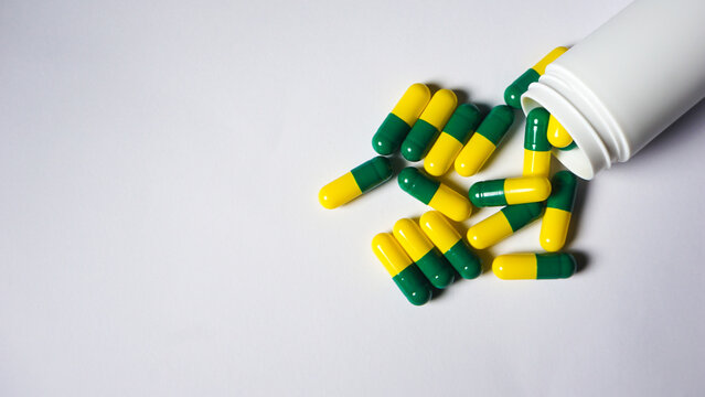 Top view of some green yellow capsules spilled from bottle to white background. 