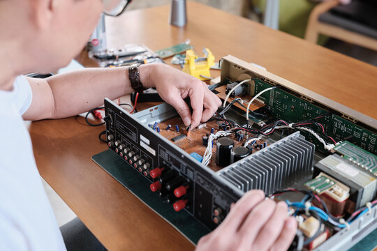 Close-up, man's hand disassembling and examining audio equipment, checking circuit board for repair, home electrical appliance DIY fix and maintenance, electronics component hobby, handyman workshop.