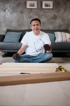Portrait of Asian mature man preparing flat-pack furniture parts, cheerful smile, self-assembly with carpentry diy tools, home improvement, craft install hobby workshop, handyman active lifestyle.