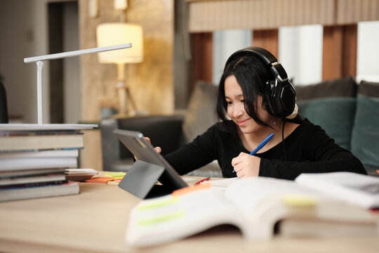 Asian teenage girl concentrates on online class, remote learning at home using tablet, writing and reading textbooks, self-study for back to school, Homeschooling, university education lifestyle.