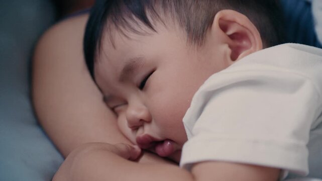 4K Video of Asian baby sleeping peacefully in mother's embrace on bed