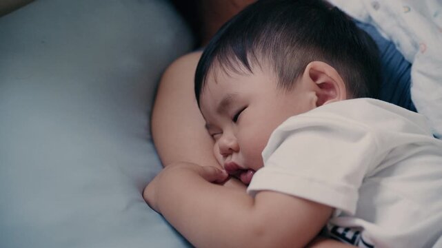 4K Video of Asian baby sleeping peacefully in mother's embrace on bed