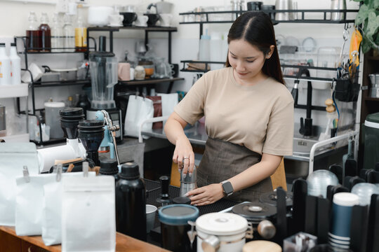 Female barista preparing coffee behind cafe counter with brewing equipment and supplies, representing coffee preparation, professional service, hospitality, small business, daily cafe workflow.