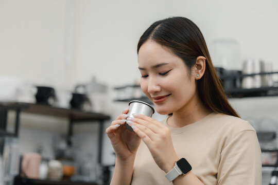 Female barista smelling coffee beans in stainless steel cup at cafe, checking aroma and freshness during coffee preparation. barista, coffee, aroma, beans, tasting.
