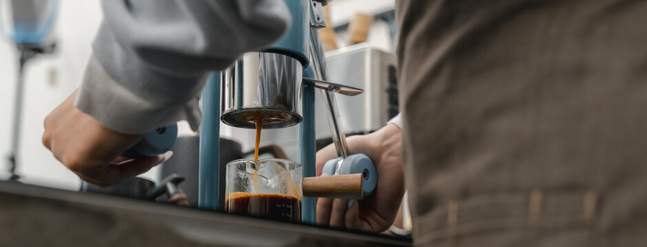 Barista brewing fresh espresso with manual coffee maker at cafe counter, extracting rich coffee into glass cup. barista, coffee, espresso, brewing, extraction.