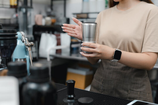 Female barista mixing coffee with stainless steel shaker behind cafe counter, preparing fresh beverage for customer service. barista, coffee, mixing, cafe, beverage.