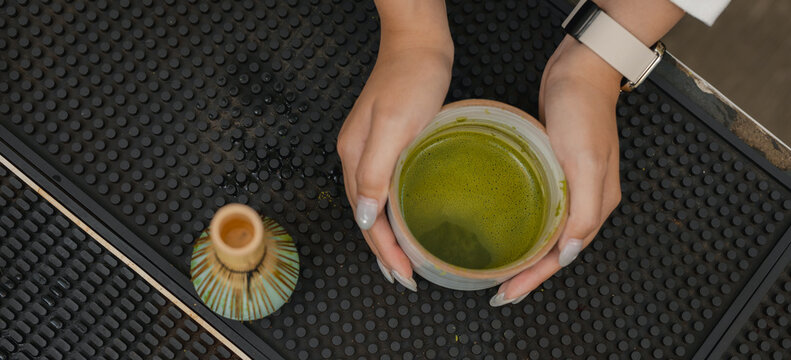 Barista holding freshly whisked matcha tea in ceramic bowl at cafe counter, showing smooth green foam beside bamboo whisk. matcha, tea, whisking, barista, beverage.