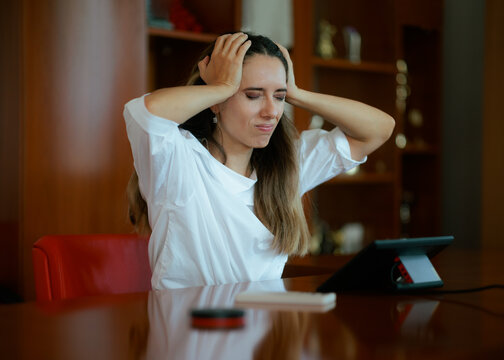Stressed Businesswoman Suffering a Migraine At her Office Desk. Exhausted woman in white shirt holds her head while sitting at desk
