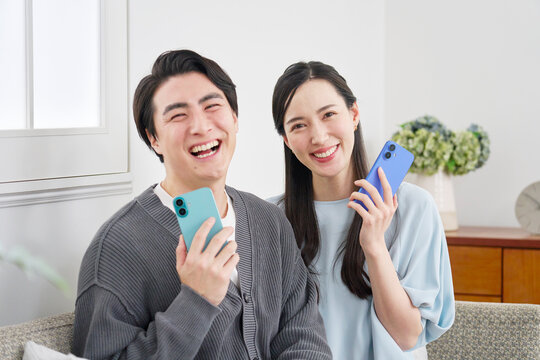 リビングでスマホを持っているカップルのポートレート　カメラ目線