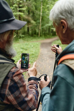 Vertical shot of Caucasian senior men checking navigation app on smartphone while hiking in forest. Imagery suitable for outdoor recreation, retirement lifestyle, and travel technology ads