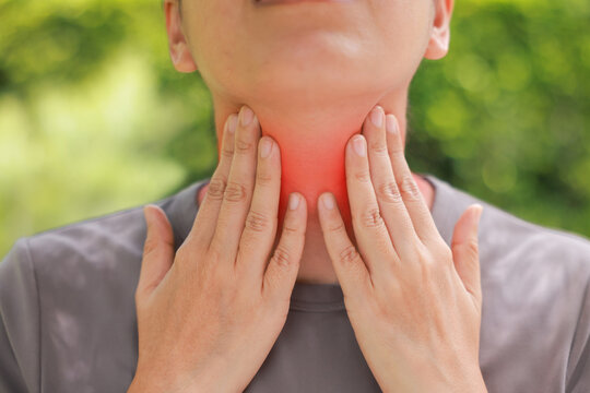 Close up of woman touching her sore throat with both hands, red highlighted area indicating severe pain, thyroid gland problems, inflammation, or tonsillitis symptom. Healthcare and medical concept.