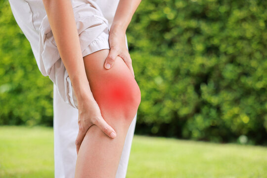 Close up of person bending and holding bare knee with red highlighted area indicating severe joint pain, arthritis, muscle ache or sports injury. Healthcare, medical, and physical therapy concept.