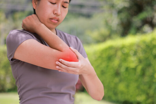 Close up unhappy Asian woman touching her elbow with a red highlighted area indicating severe joint pain, arthritis, muscle ache or sports injury. Healthcare, physical therapy, and medical concept.