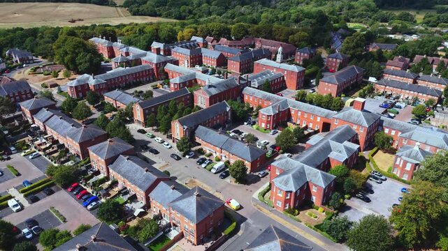 Aerial drone view of Knowle Village near Fareham, Hampshire, featuring converted Victorian red-brick former hospital buildings and modern residential housing surrounded by green fields.