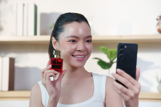Asian woman holding perfume bottle and recording smartphone video for beauty vlog