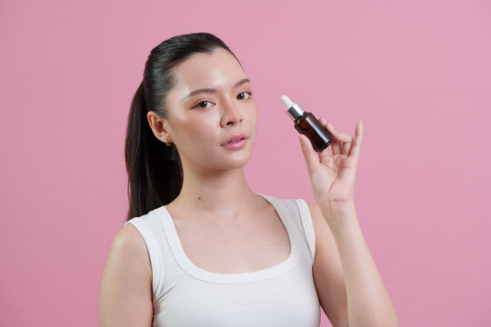 Asian woman holding serum dropper bottle for skincare and beauty treatment
