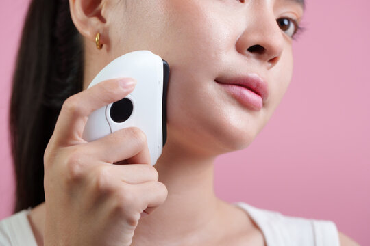 Asian woman using electronic facial massager on cheek for skincare and facial beauty routine