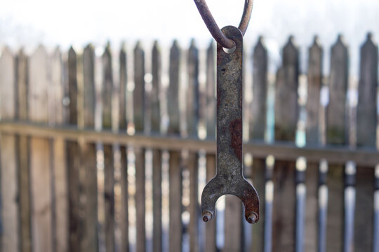 Rusty pin spanner hanging from a metal hook in front of a blurred wooden fence