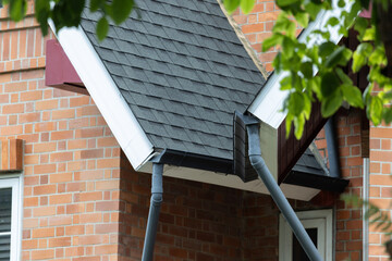 Black rain gutters drain water from a house roof © Rattanachat