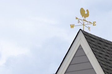 Rooster weather vane on house peak, gray siding, white trim, overcast sky © Rattanachat