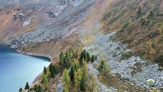 Horizontal aerial drone video gliding over a rocky mountain slope and the shore of a deep blue alpine lake.