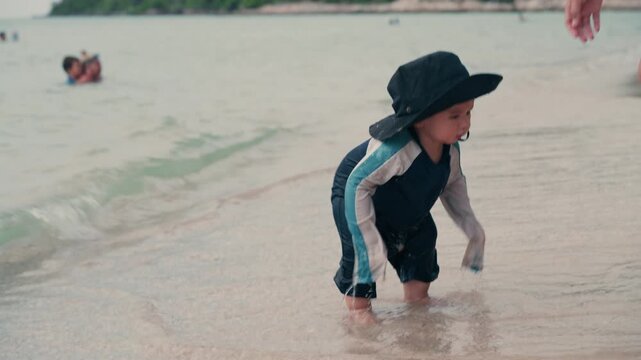 Asian Baby in Swimwear with Black Hat Playing and Walking on Beach with Mother, Family Beach Day, Summer Vacation