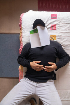A vertical, top-down view of a man lying in bed who has fallen asleep with an open book resting on his face