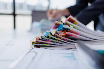 Busy office worker organizing a large pile of documents and paperwork with colorful binder clips,...
