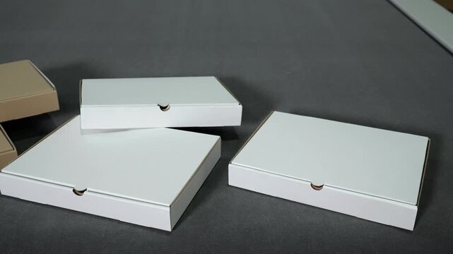 Four takeaway cardboard boxes with kraft brown bodies and white lids on dark matte surface, neatly arranged in diagonal layered layout for packaging and delivery presentation