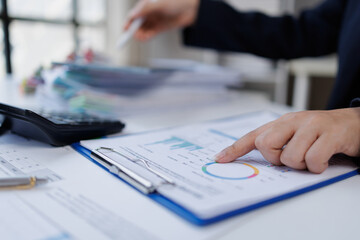 Person's hand pointing at a colorful pie chart on a clipboard, engaging in data analysis and...