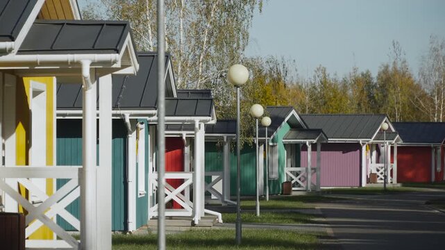 Alley with small multicolored wooden houses on sunny autumn day. Recreation base, glamping with comfortable conditions for escape from urban bustle during autumn holidays.