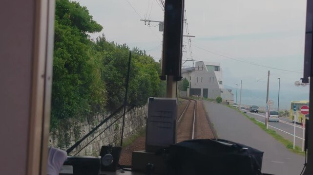 Enoshima Electric Railway travels beside the coast in Kanagawa, Japan, with tracks running parallel to the ocean and coastal highway during a scenic passenger journey.