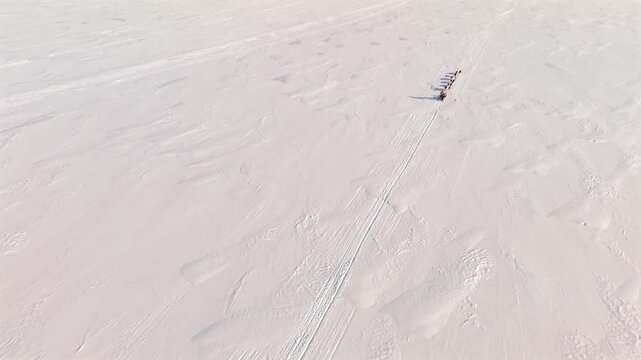 Aerial push forward over a vast empty snowfield in Svalbard, reflecting the solitude, scale and total silence of a distant dog sled team crossing the ice