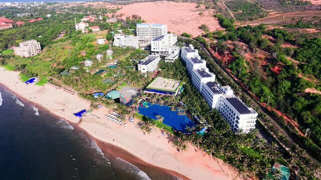 A view of Xuan Thuy in Mui Ne, Lam Dong shows the beach, resorts, and activities. The sky is clear and the sun shines on the water. Visitors can enjoy the beach and surrounding area.