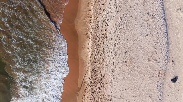 Sandy shores appear in Xuan Thuy, Mui Ne, Lam Dong. The camera shows waves touching the sand while people walk by. The colors of the sand and water change in the sunlight.