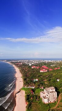 Clear skies and bright sun showcase the coastline in Xuan Thuy, Mui Ne, Lam Dong. The beach stretches along the shore with buildings dotting the landscape. People enjoy the day by the water.