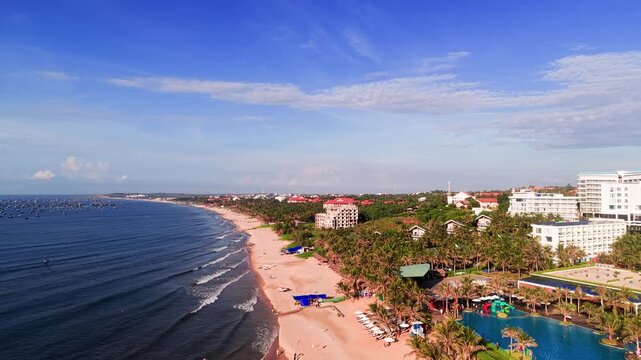 View the coastline of Xuan Thuy in Mui Ne, Lam Dong during a sunny day. Observe the beach, sand, and waves as people relax and enjoy the surroundings near the water.