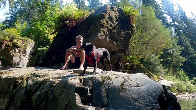POV view of a man and dog sitting on a large boulder in Inter River Canyon in North Vancouver, British Columbia, Canada