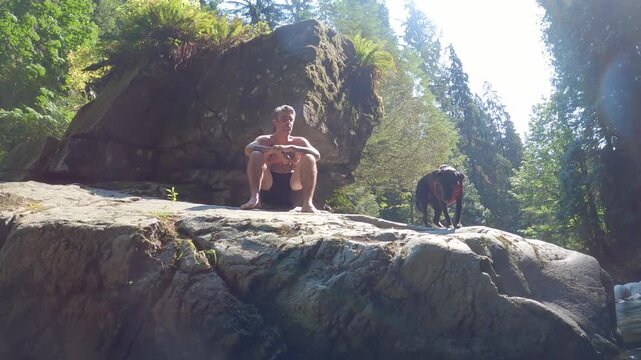 A man and his dog sit on a large rock boulder in Inter River Canyon in North Vancouver, British Columbia, Canada