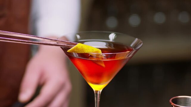 Close up shot of a professional bartender's hands carefully placing a fresh citrus peel twist on the edge of an elegant cocktail glass as a finishing garnish at a premium bar