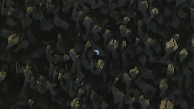 Kite surfer across dark coastal surface at Stokksnes beneath Vestrahorn mountain area, with patterned volcanic terrain visible from directly overhead, drone top down descent.