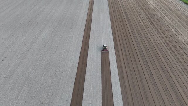 Agricultural tractor follows precise parallel passes, creating uniform soil bands across cultivated fields, illustrating GPS guided precision farming and mechanized soil preparation in Po Valley Italy