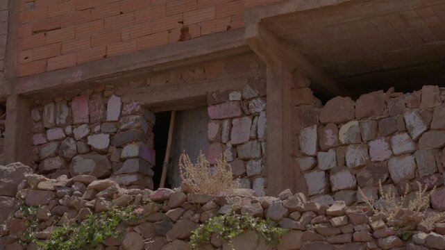 Hand-chiseled stone walls meet modern terracotta brick and concrete beams on a hillside house, highlighting rustic vernacular building techniques in a remote High Atlas Berber village in Morocco.