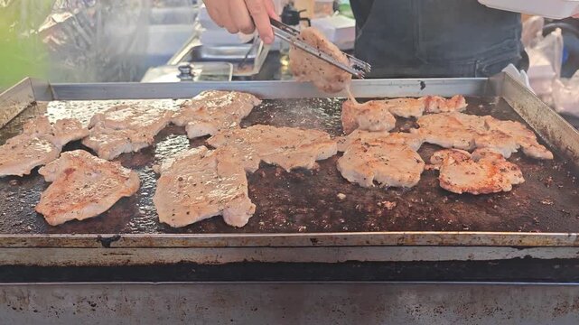 Close Up of Worker Grilling pork on a Grill to make steak Outdoors with Fire,street food Outdoor Cooking and walking street Food Preparation Concept.