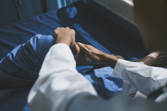 Asian male doctor examining foot of female patient sitting on bed in hospital room. Performing medical checkup. Diagnosing injury. Providing healthcare. Podiatry. Physical therapy. And rehabilitation