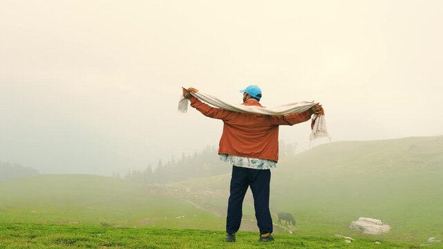Man standing on a mountain meadow near Rudranath Temple in Chamoli holding a scarf in the wind